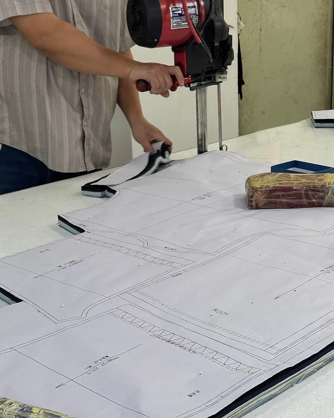 A cutter guiding a straight-knife machine through a paper marker pinned over stacked fabric